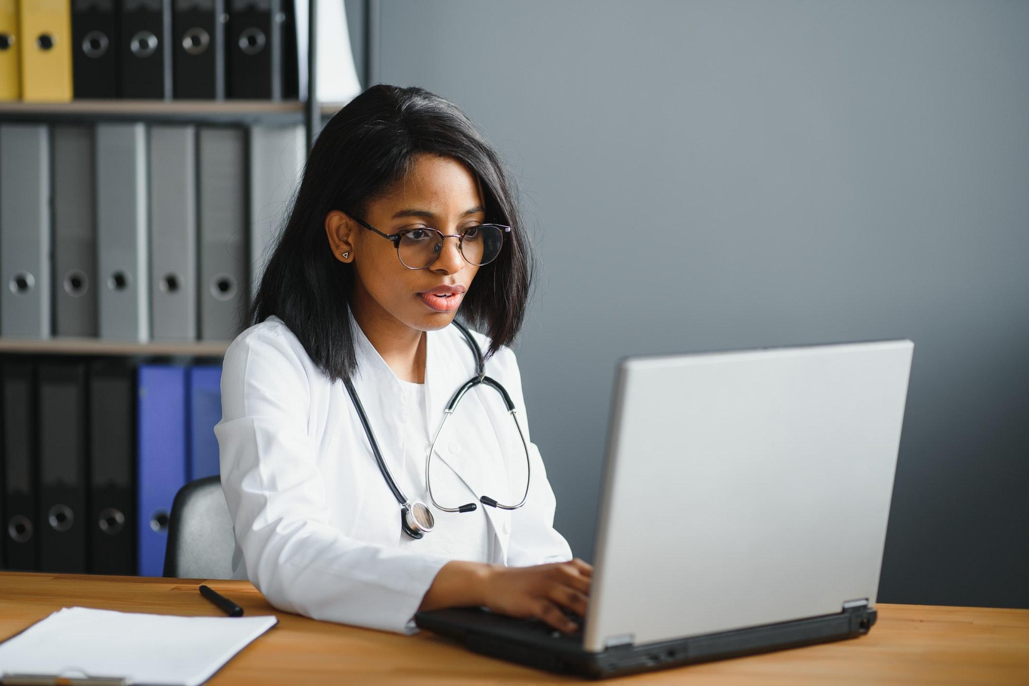 healthcare, medical and technology concept - african female doctor with laptop