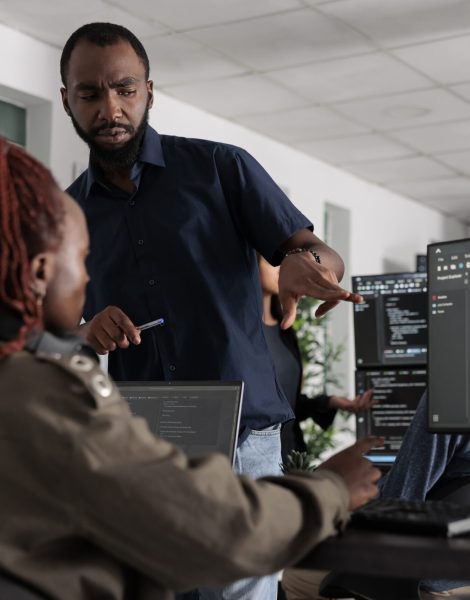 African american engineers typing machine learning html code on computer, sitting at desk table in big data office. Software developers working on database system with html script in it security agency.